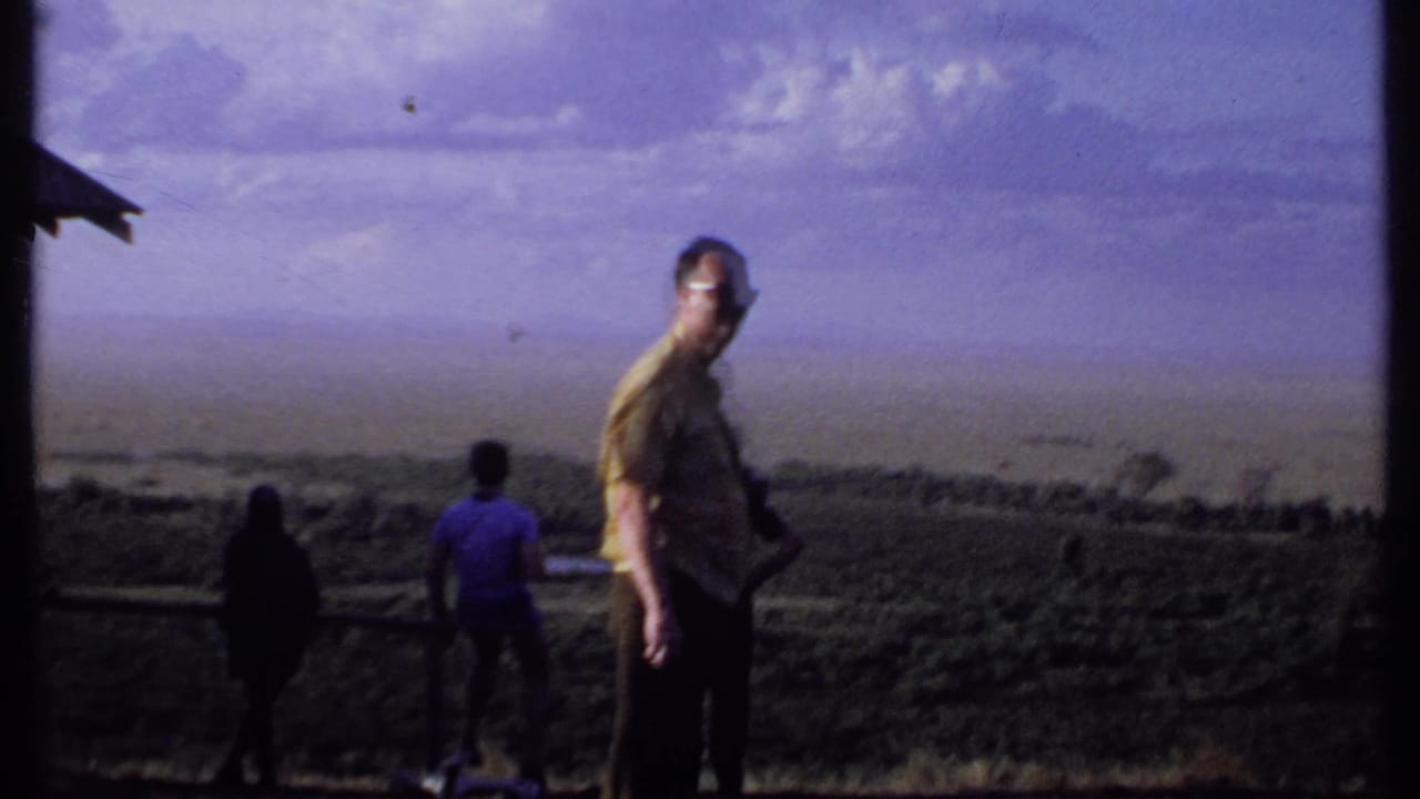 Adult men stand near a grassy overlook with open plains in the background.