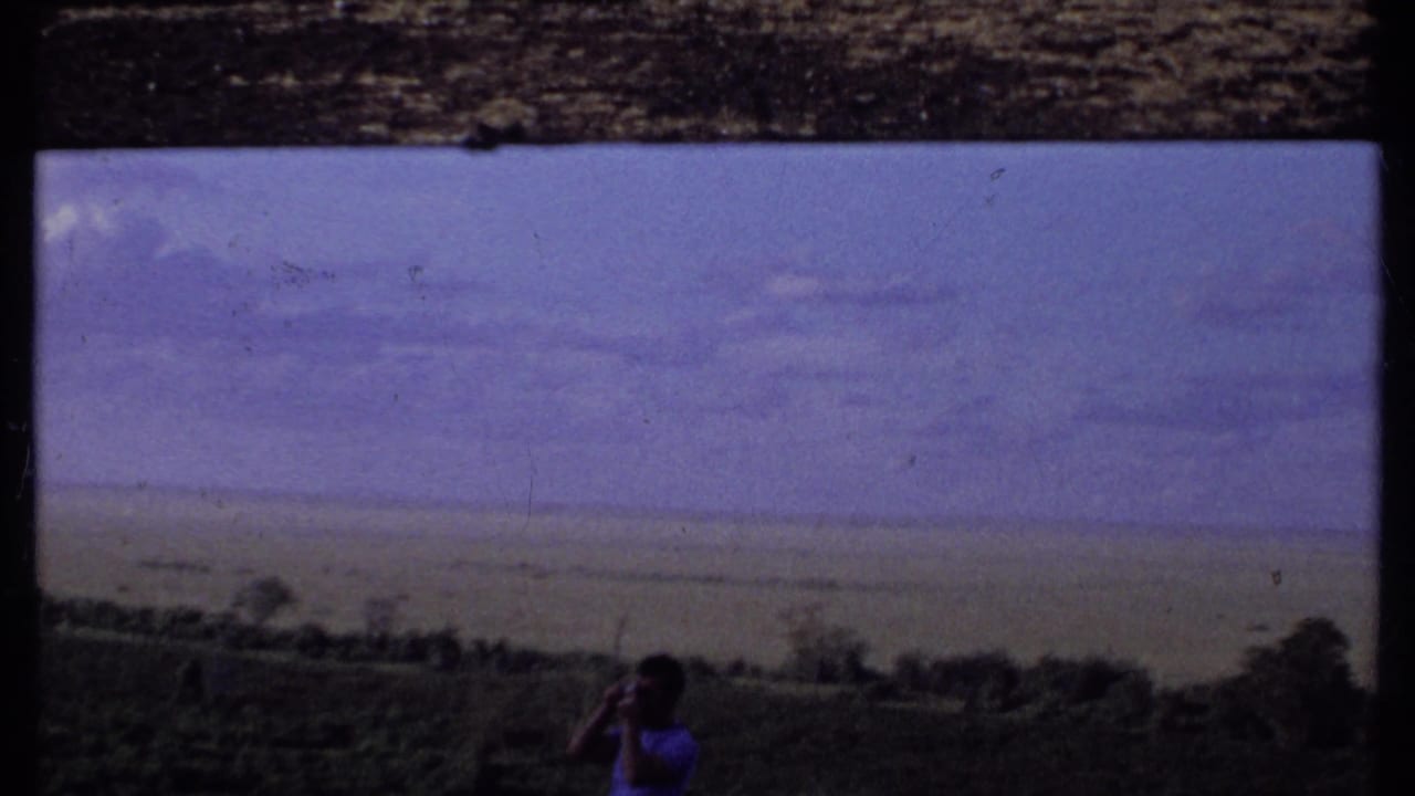 Soft 8mm frame from Kenya in 1969 with a man photographing the landscape from a dark grassy foreground.