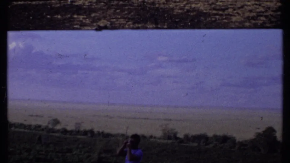 Soft 8mm frame from Kenya in 1969 with a man photographing the landscape from a dark grassy foreground.