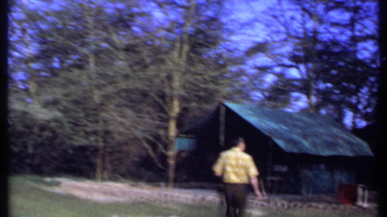 Man continues walking toward a large green tent beside trees and grass.
