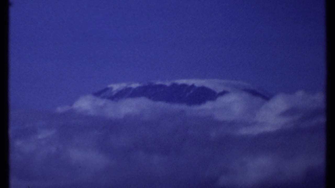 Snow-capped mountain summit emerging above clouds under a deep blue sky.