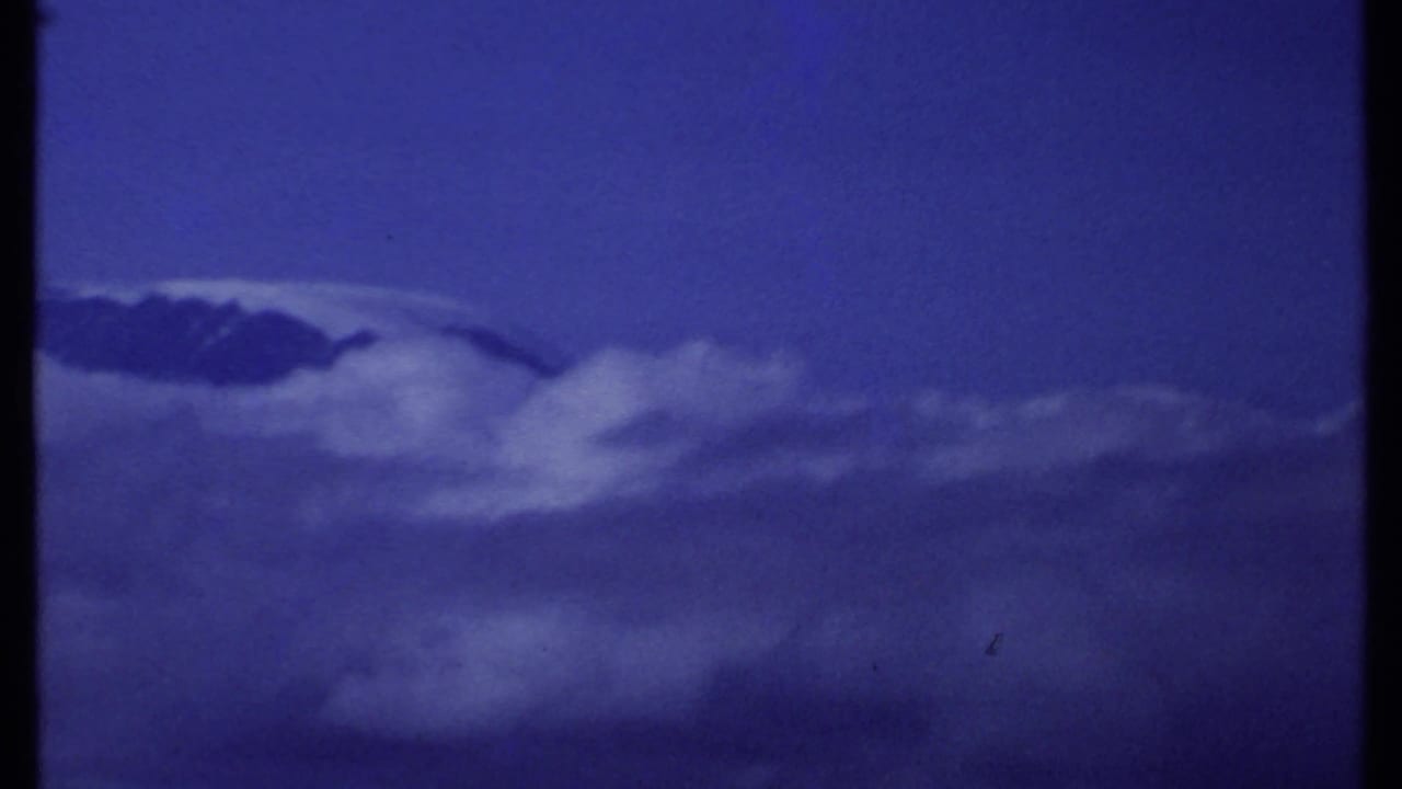 1969 Kenya 8mm frame with the mountain summit partly at the edge of view, surrounded by broad cloud layers.