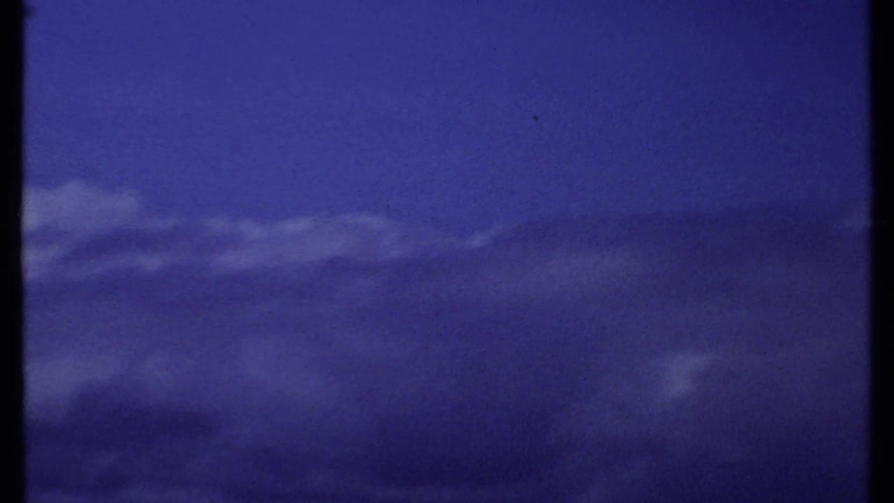 1969 Kenya 8mm aerial cloudscape with the mountain largely hidden or outside the frame beneath a saturated blue sky.