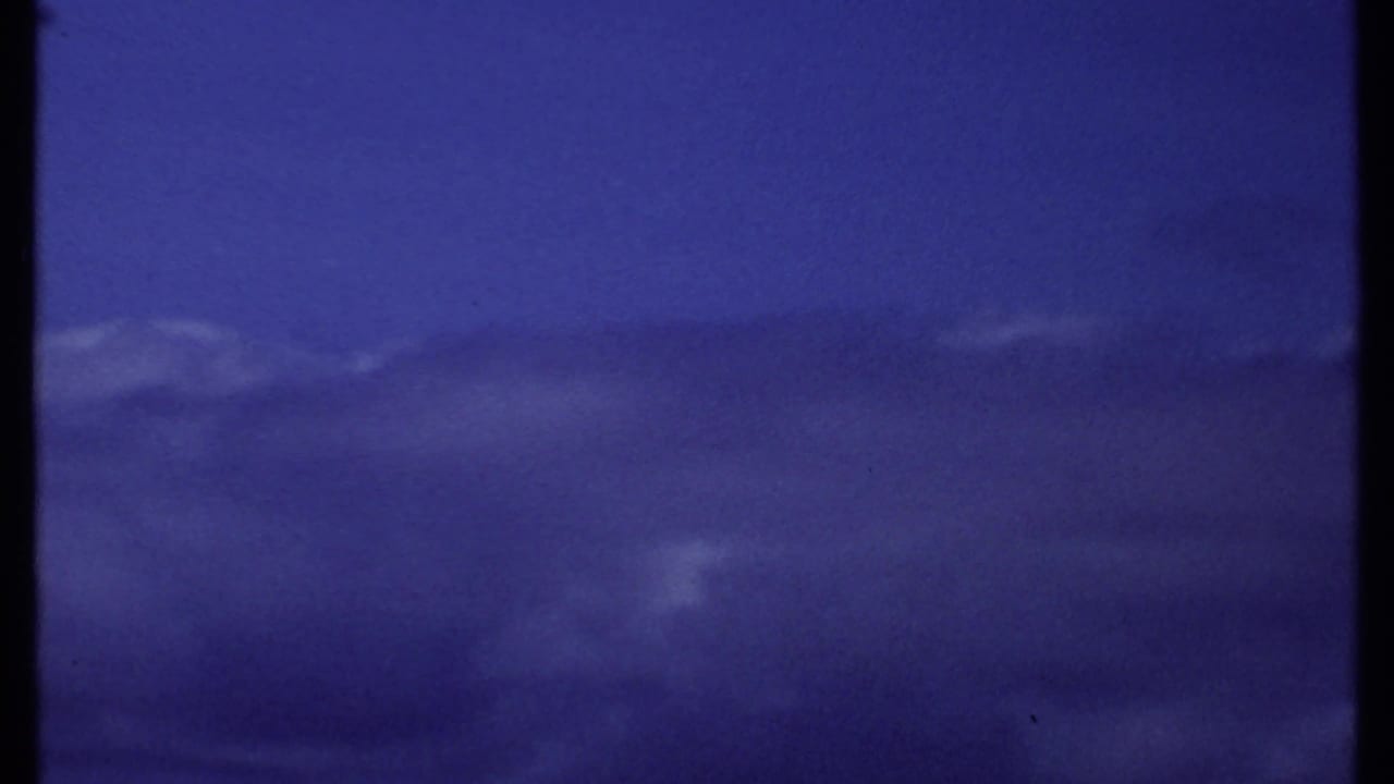 Dark blue overcast sky above a faint ocean horizon with film grain and frame edge.