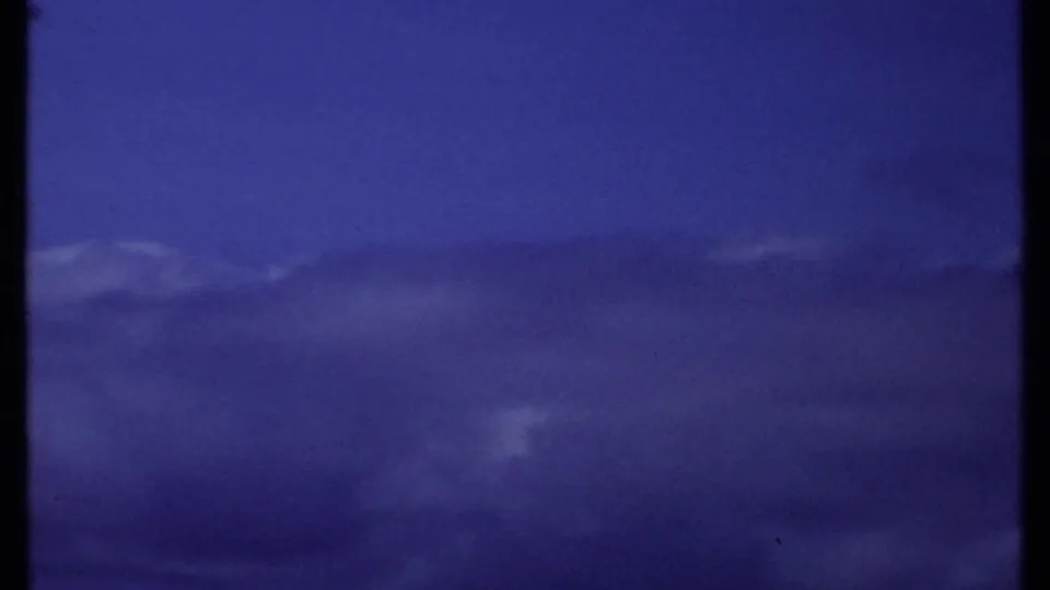 1969 Kenya home-movie frame showing blue-purple cloud cover over a distant ocean horizon, with visible 8mm grain and scan borders.
