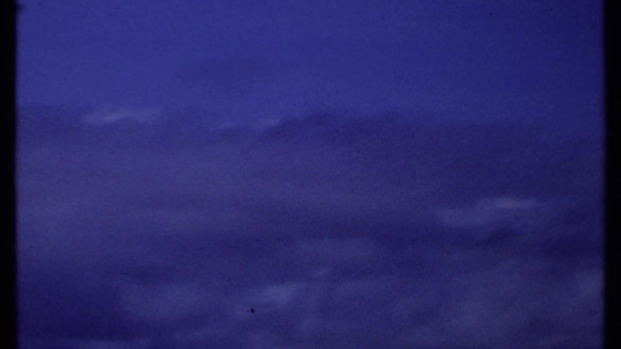 1969 Kenya coastal sky view with layered clouds and a distant ocean line, partially interrupted by a dark vertical film or scan border.