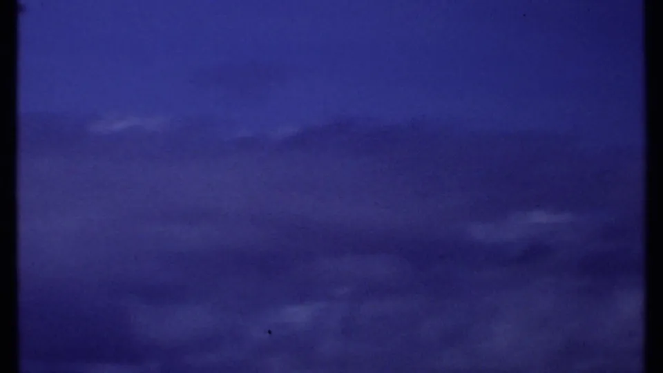1969 Kenya coastal sky view with layered clouds and a distant ocean line, partially interrupted by a dark vertical film or scan border.