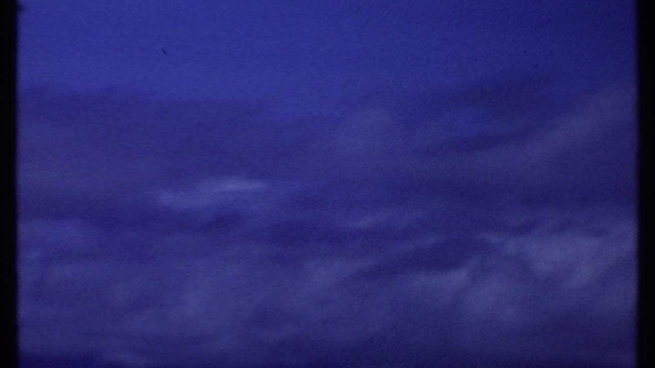 1969 Kenya home-movie frame of a saturated blue coastal sky, low cloud streaks, and a dark horizon band near the bottom edge.