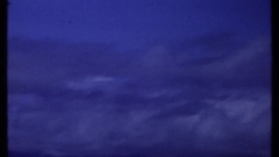 1969 Kenya home-movie frame of a saturated blue coastal sky, low cloud streaks, and a dark horizon band near the bottom edge.