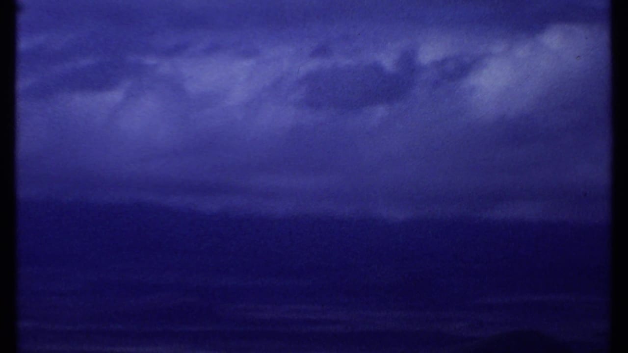 1969 Kenya coastal view showing cloud layers above a dark ocean or shoreline band, rendered in saturated small-gauge film color.