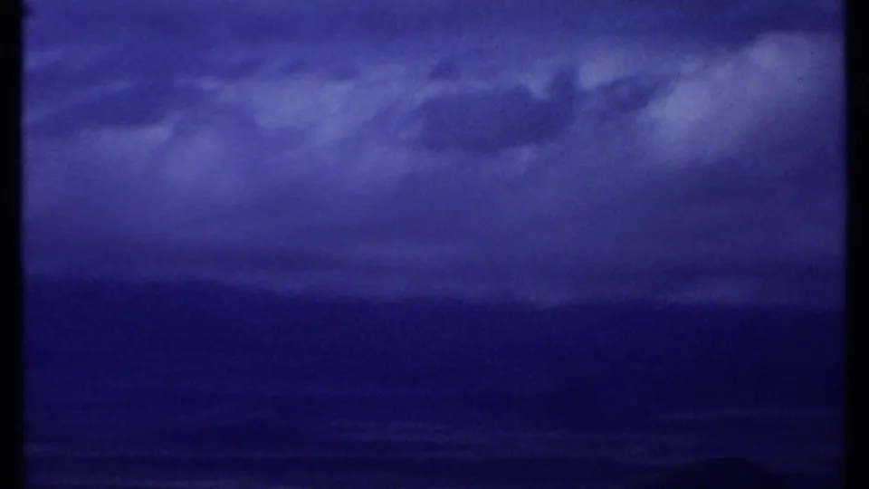 1969 Kenya coastal view showing cloud layers above a dark ocean or shoreline band, rendered in saturated small-gauge film color.