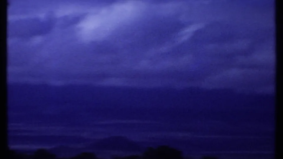 1969 Kenya 8mm frame showing a deep blue clouded sky over a dark, distant tree line.