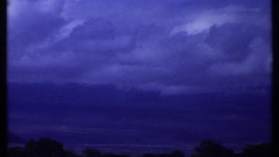 1969 Kenya home-movie frame with layered blue clouds and a silhouetted tree line near the lower edge.