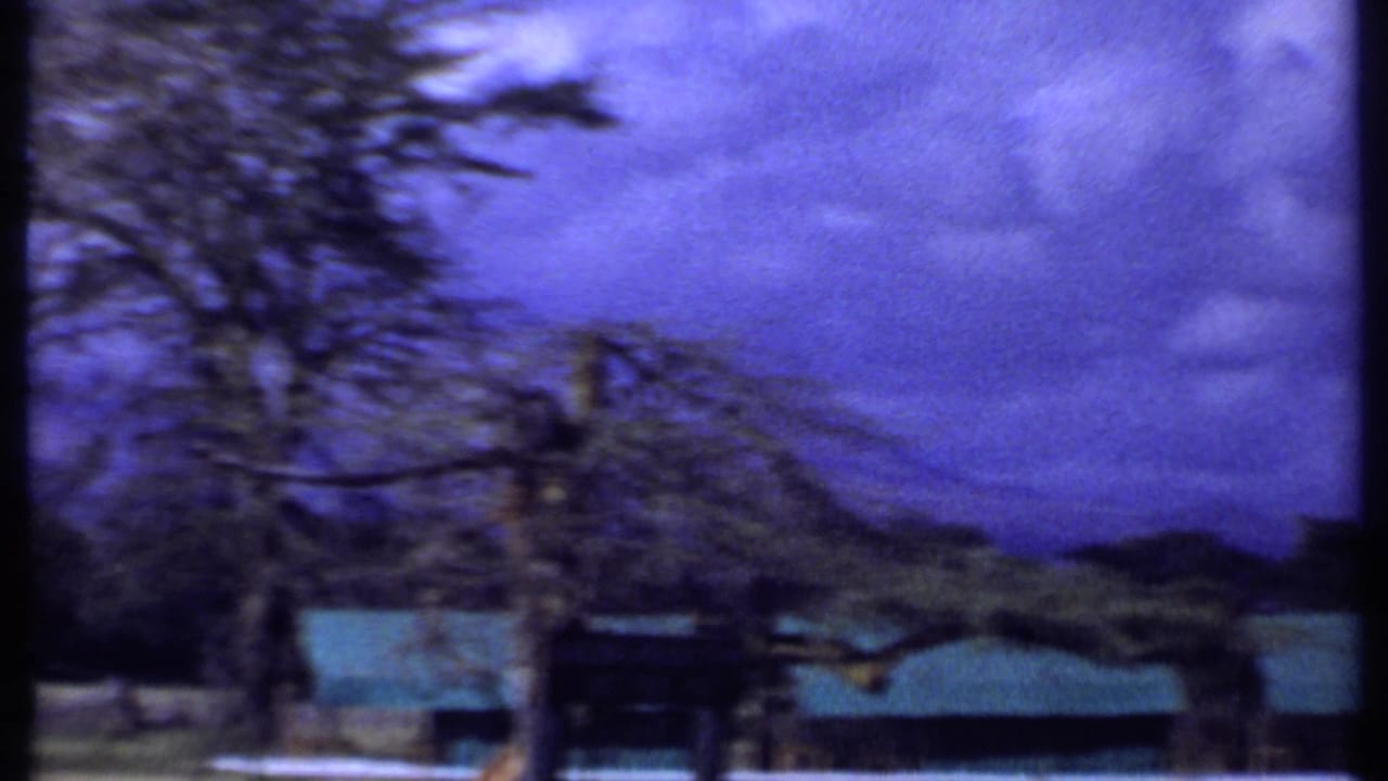 Green-roofed low buildings behind white fencing under a blue clouded sky.