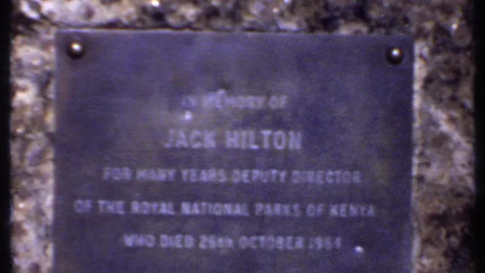 1969 Kenya frame showing a memorial plaque for Jack Hilton mounted on stone, with soft focus and blue-purple color shift.
