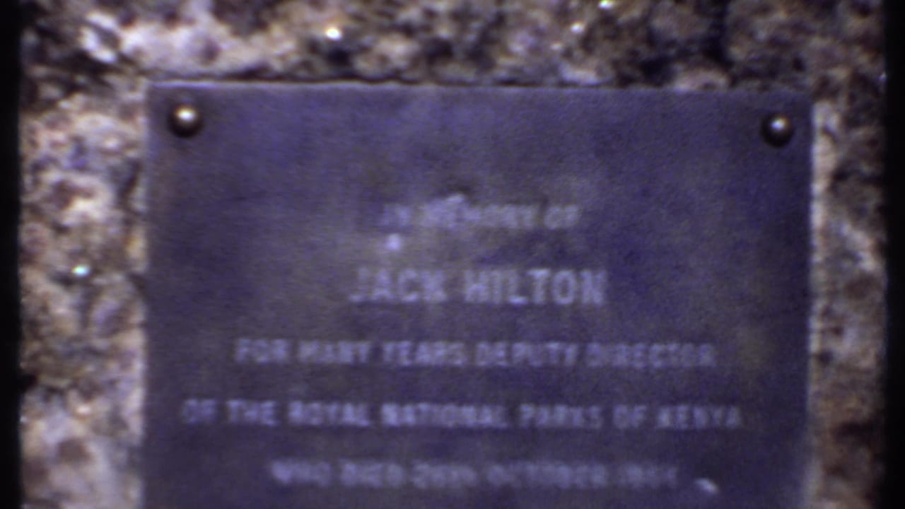 Close 1969 Kenya home-movie view of the Jack Hilton memorial plaque, with Royal National Parks of Kenya text partly legible.