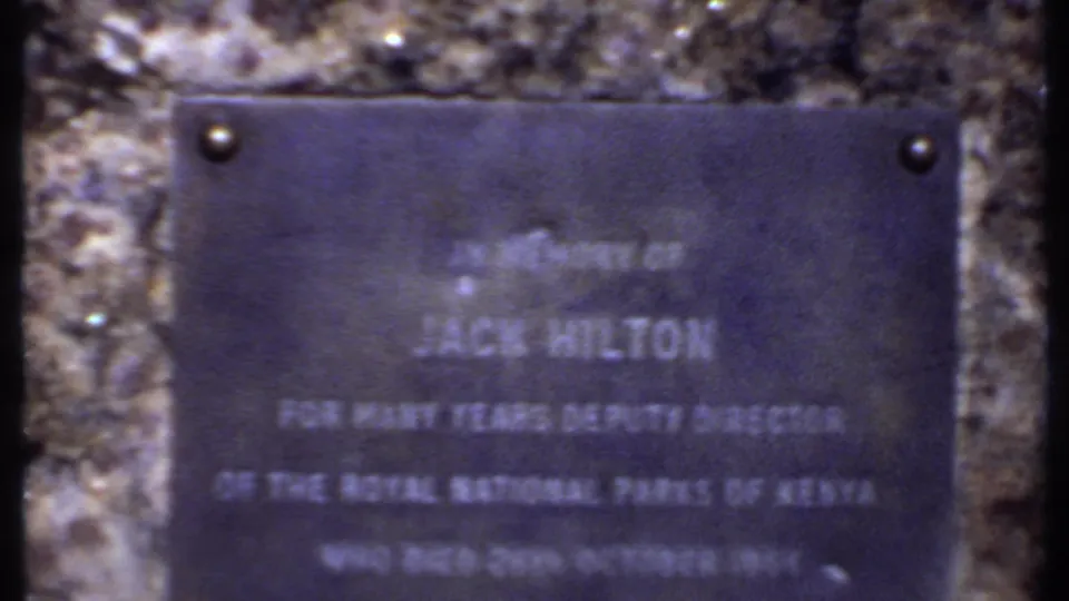 Close 1969 Kenya home-movie view of the Jack Hilton memorial plaque, with Royal National Parks of Kenya text partly legible.