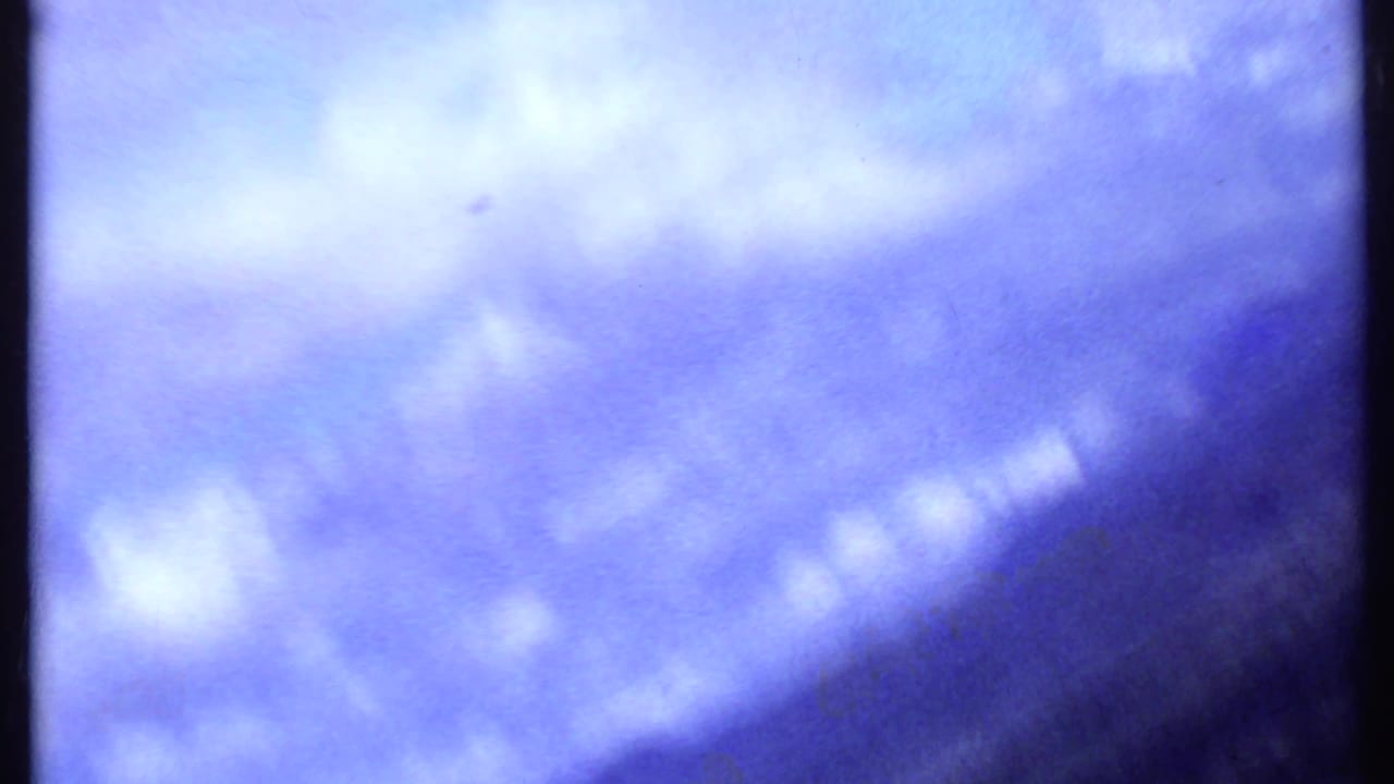 1969 Kenya home-movie frame of blue-purple sky and pale clouds, with film grain and a dark edge intruding at the lower right.