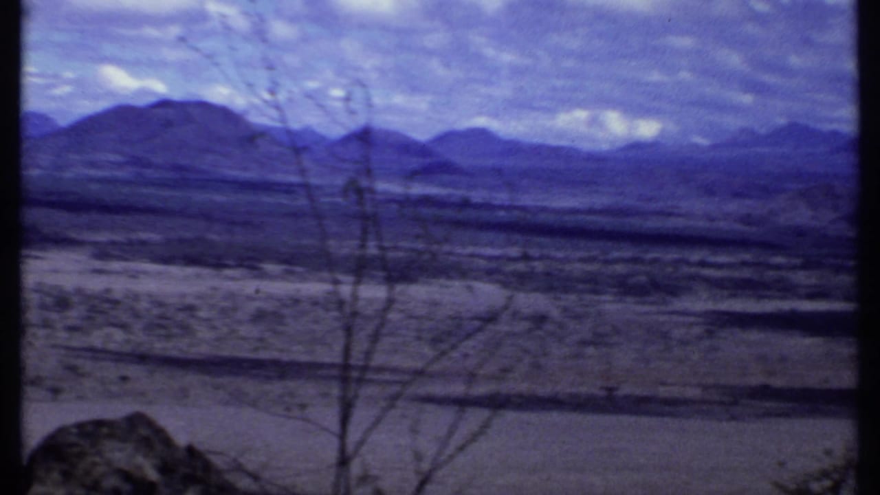 Wide dry landscape with distant mountains under a cloudy sky.