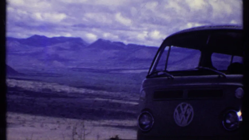 1969 Kenya home-movie frame with the front of a Volkswagen bus at right and dry mountain landscape beyond.