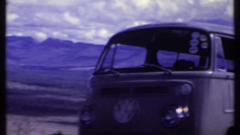 Kenya 1969 home-movie frame showing the front of a Volkswagen bus parked in open arid terrain beneath a cloudy sky.