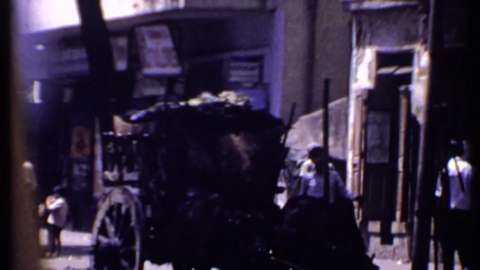 1969 Kenya 8mm frame showing a covered street cart near building entrances, with several pedestrians partly obscured by shadows and foreground shapes.