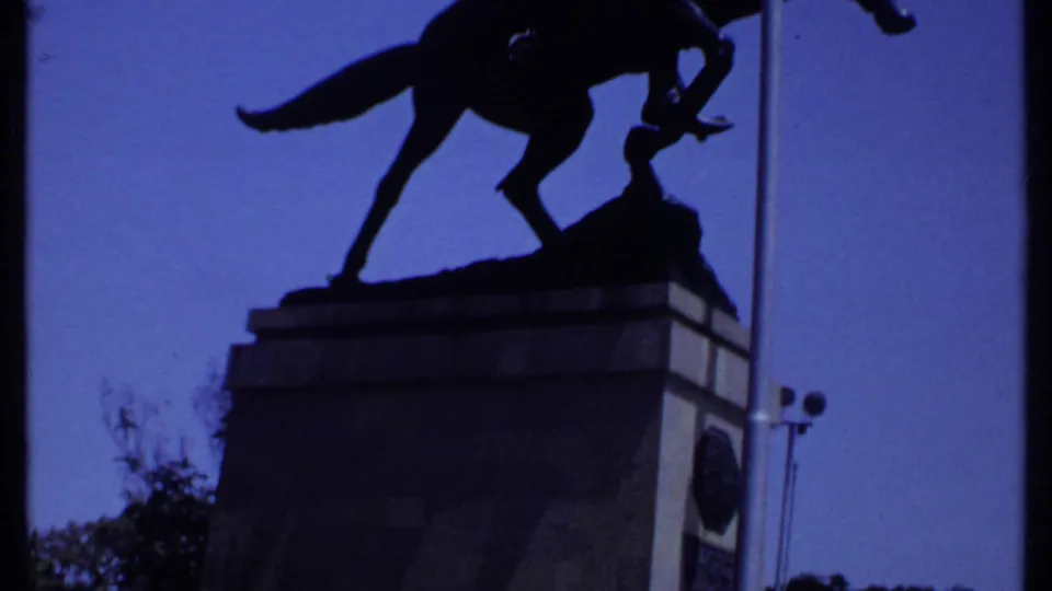 1969 Kenya 8mm frame showing the silhouetted mounted statue above a stone pedestal with trees below.