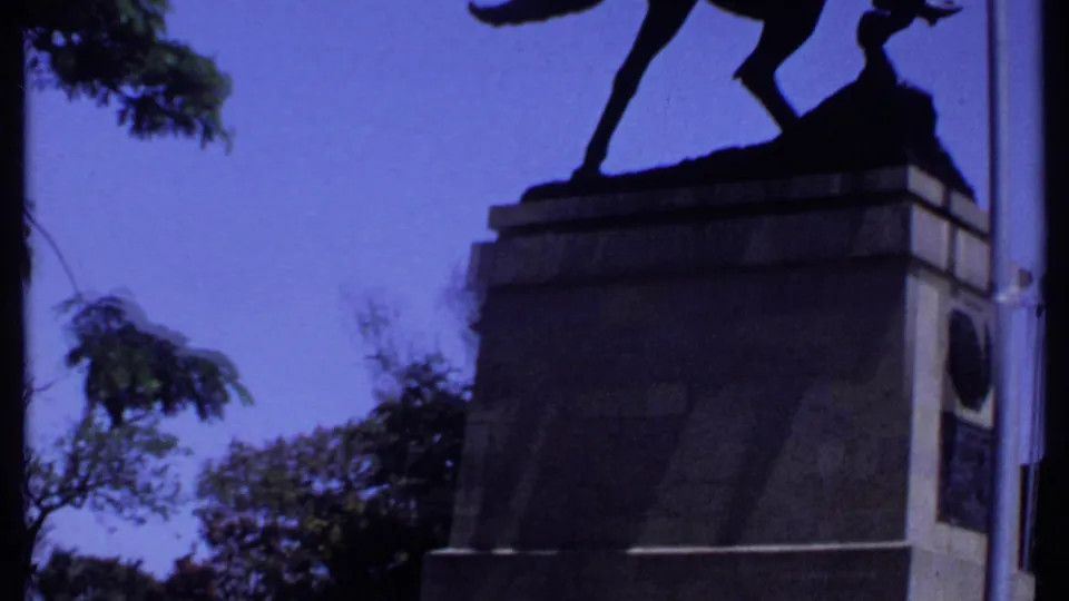 1969 Kenya frame showing the statue’s horse legs and pedestal, with trees and blue sky behind.