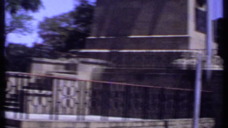 1969 Kenya 8mm frame with motion blur across stone steps, a monument base, iron railings, and surrounding trees.