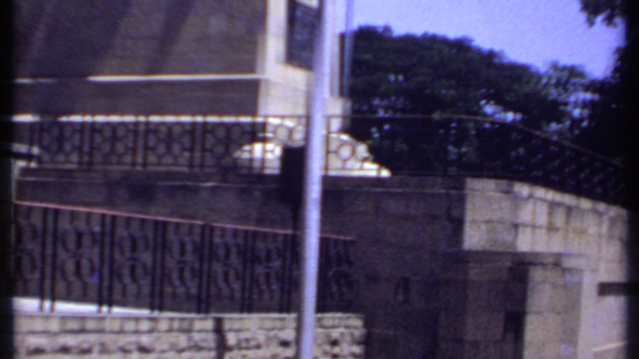 1969 Kenya 8mm frame showing stone walls, ornate railings, trees and a sunlit park edge.