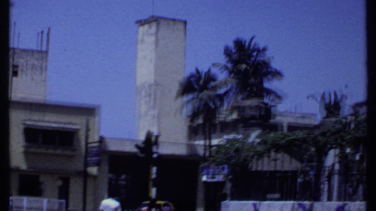 Low-rise building with a tall pale tower and palm trees beside a street.