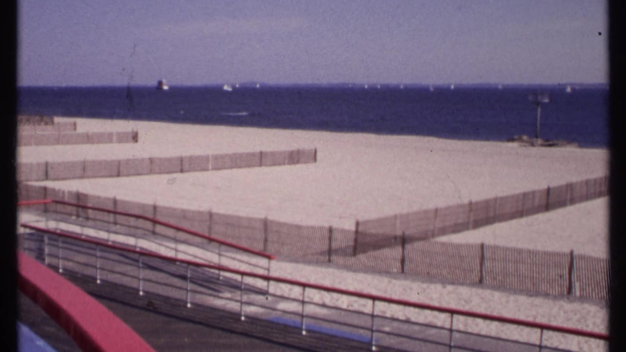 Balcony view of a divided New London beach in 1969, with pale sand, low fencing, ocean water, and small boats offshore.