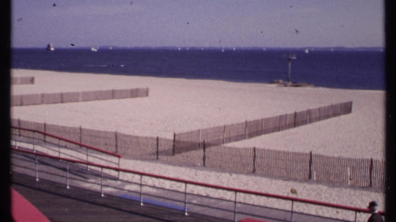 New London beach view from 1969 with fenced sand, offshore boats, balcony railings, and a partial person at the lower right edge.