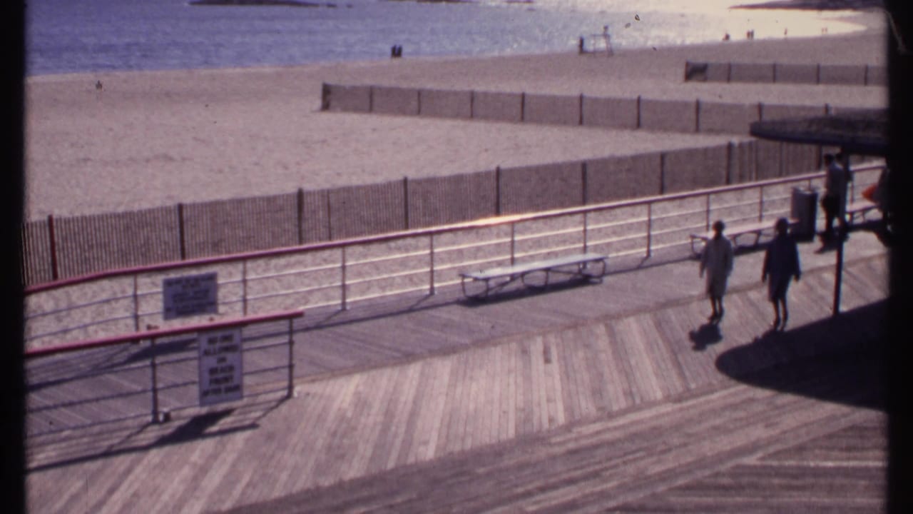 High-angle view of a beach boardwalk with two adults walking near railings and benches.