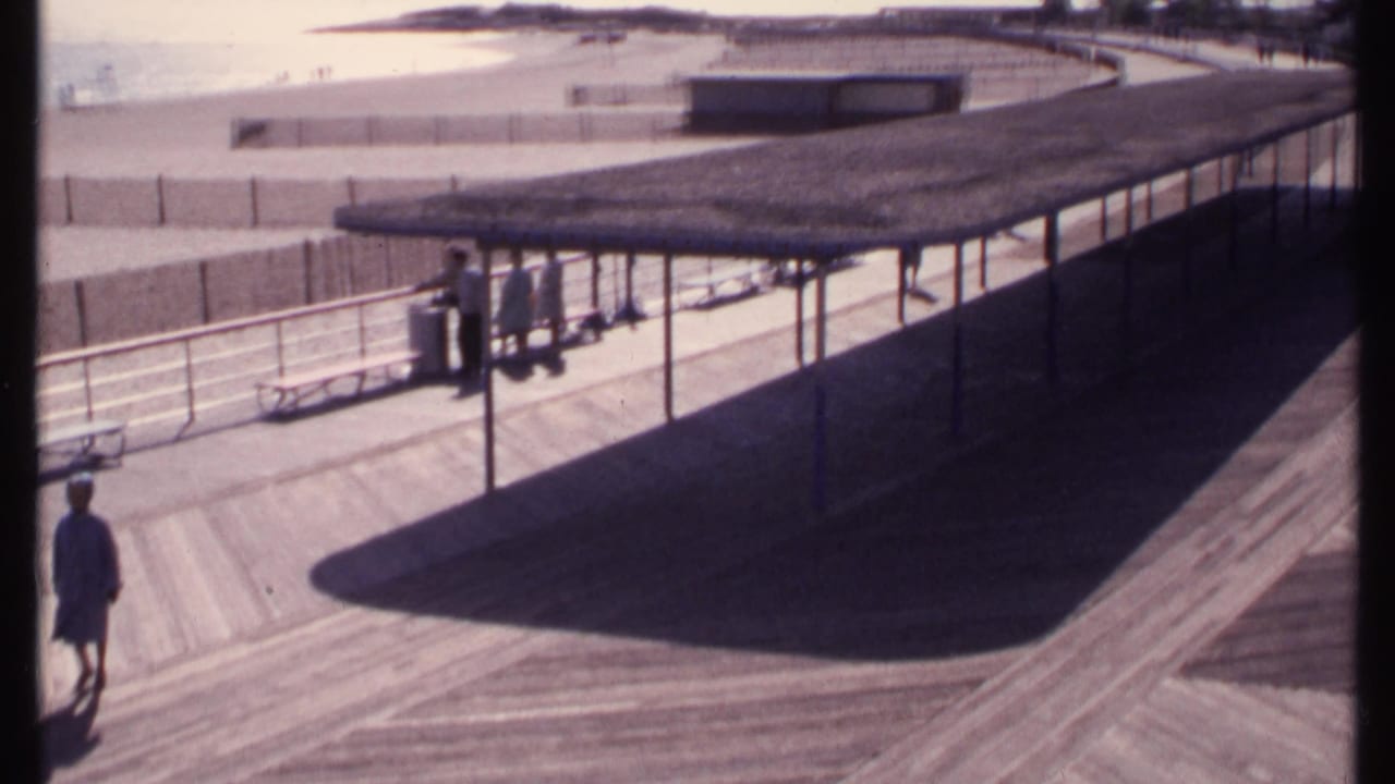 Elevated view of a covered boardwalk pavilion beside a beach with several people under the shade.