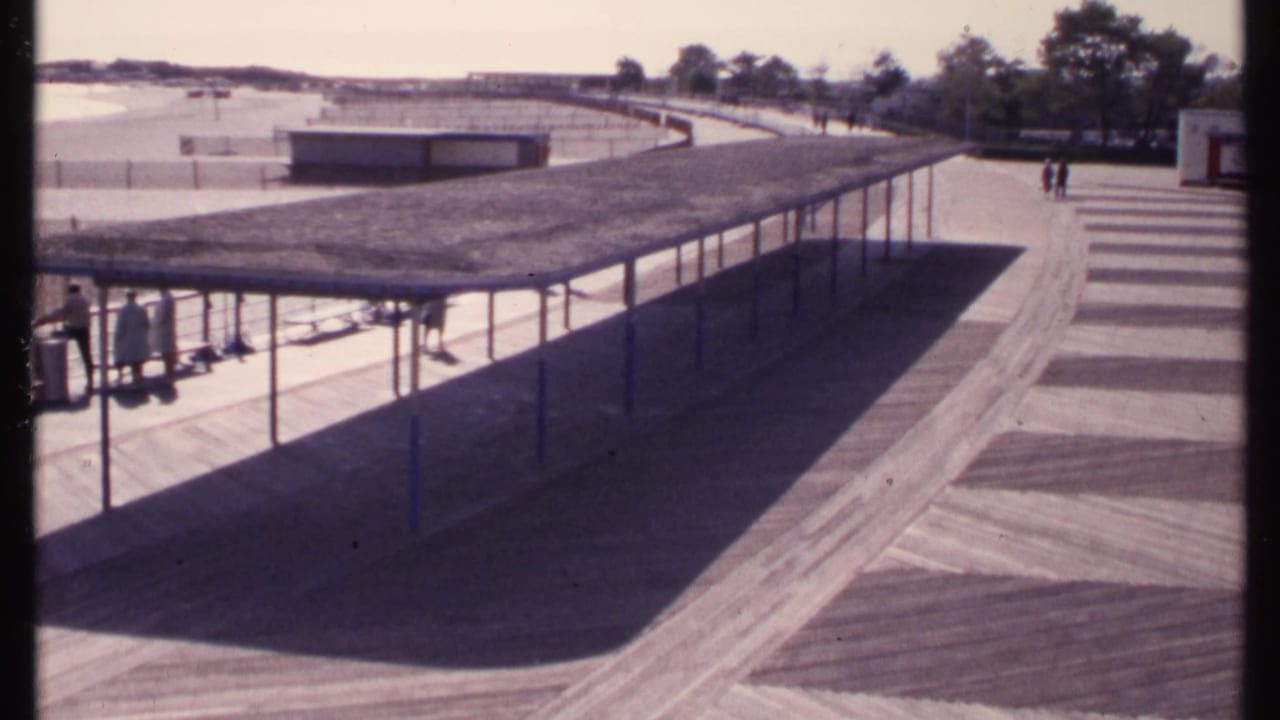 Covered walkway beside a beach area with a few people standing under the shade.
