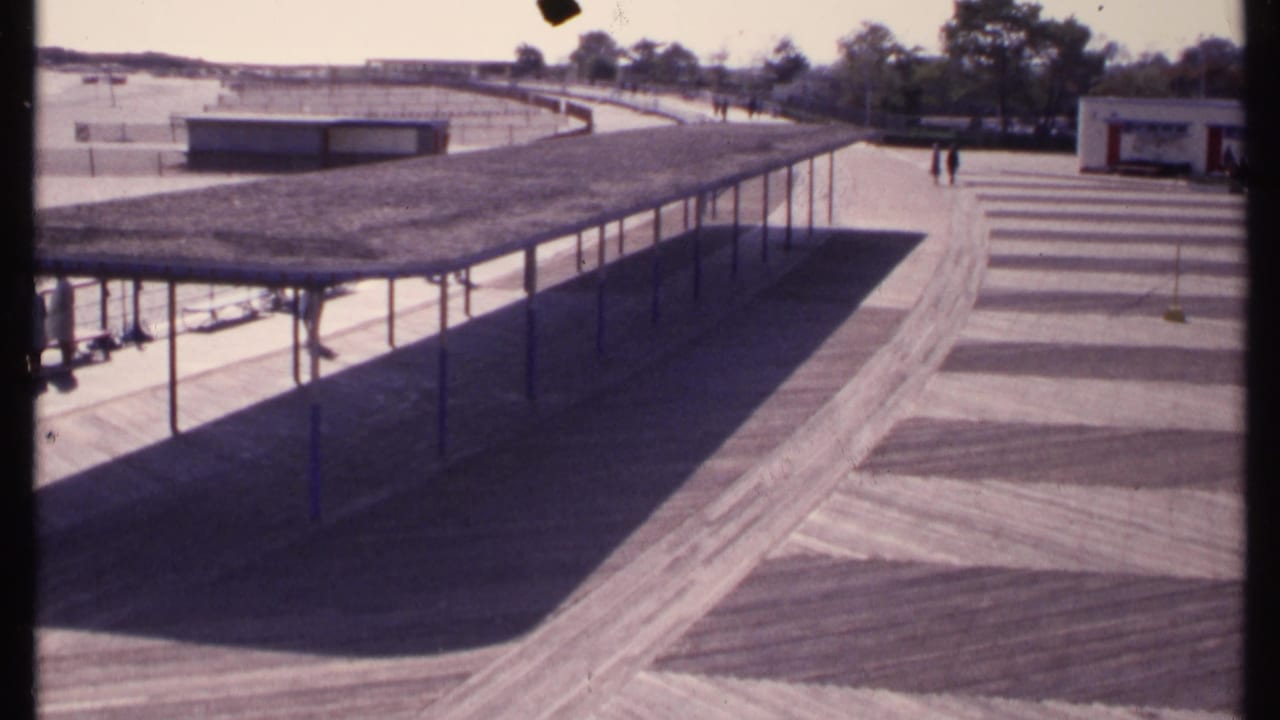 New London, Connecticut 1969 frame with a long shaded walkway, patterned pavement, beach area, low structures, trees, and small distant figures.
