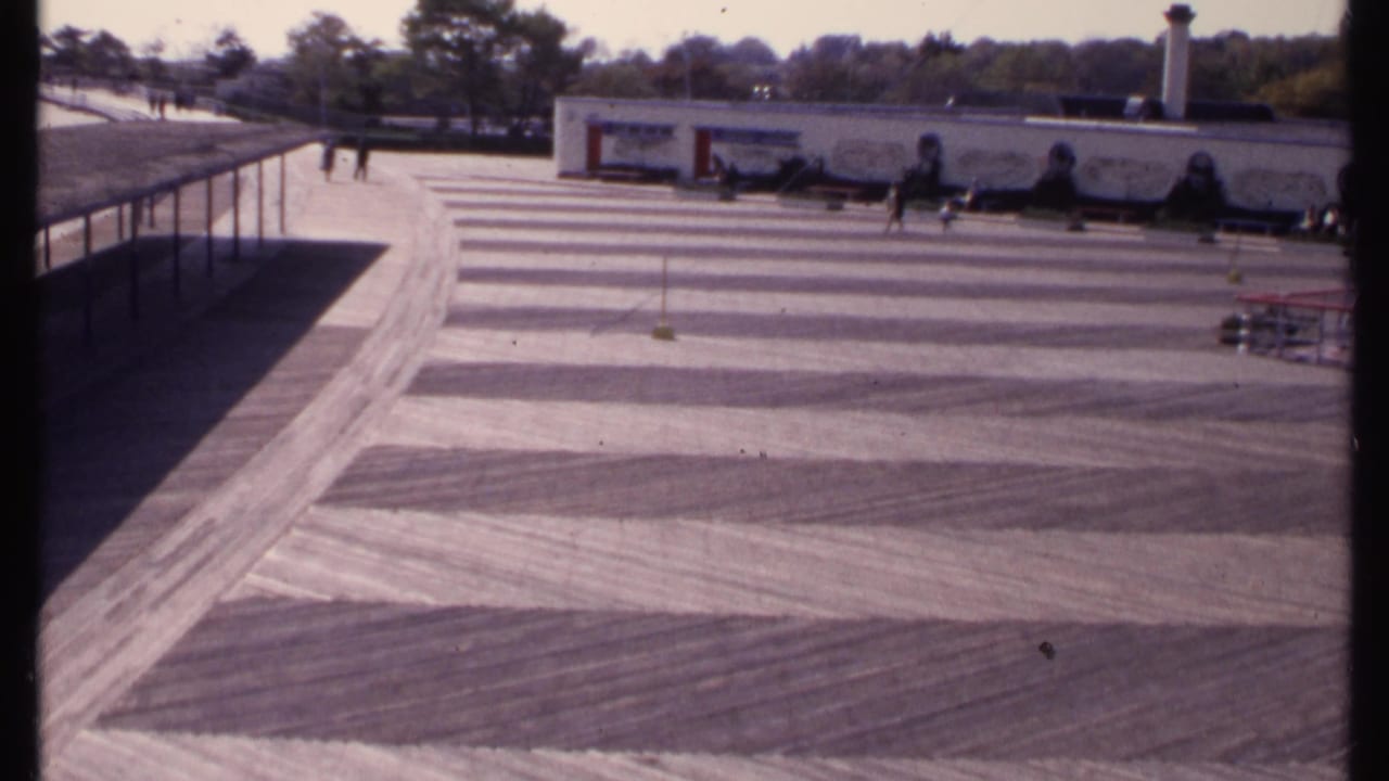 Wide patterned concrete lot with distant people near a long white building.