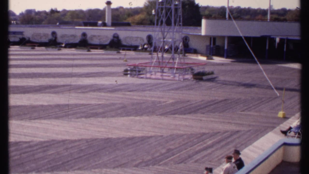 Wide outdoor deck with metal tower, low building, and seated people along a curved bench.