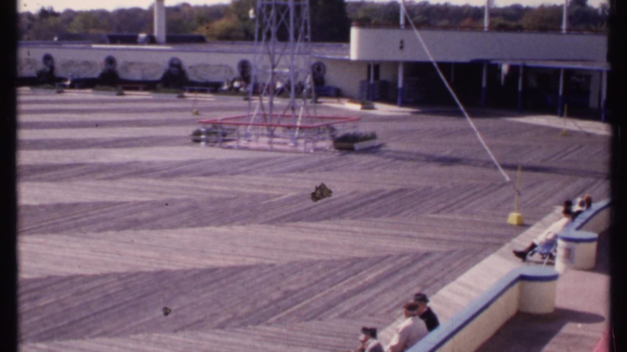 Open deck and low building with several people seated along the right-side curved bench.
