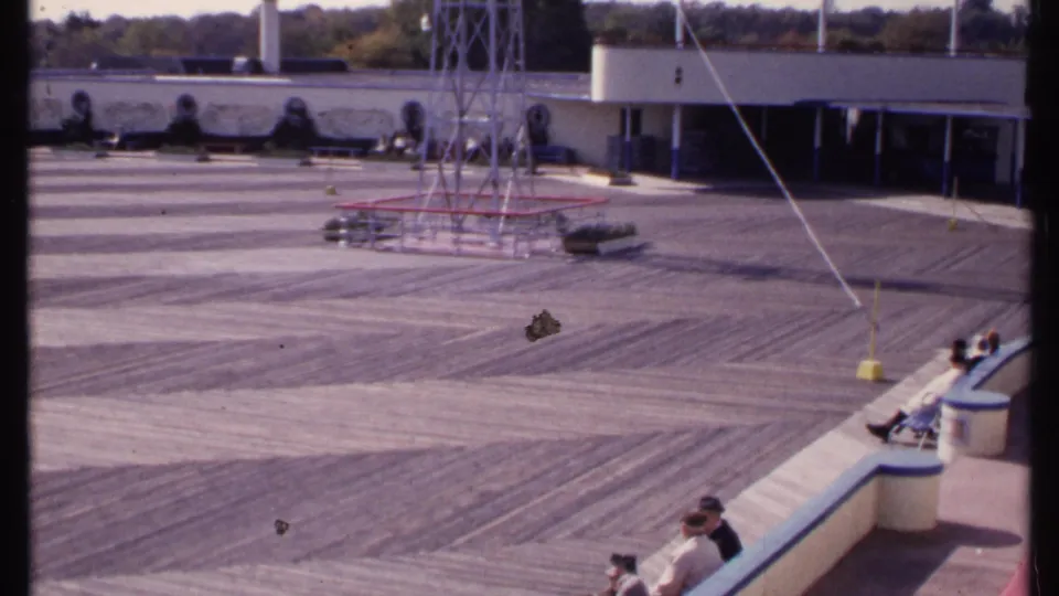 Elevated 1969 New London view across a mostly empty outdoor deck, with seated visitors near a curved bench and a low building beyond.