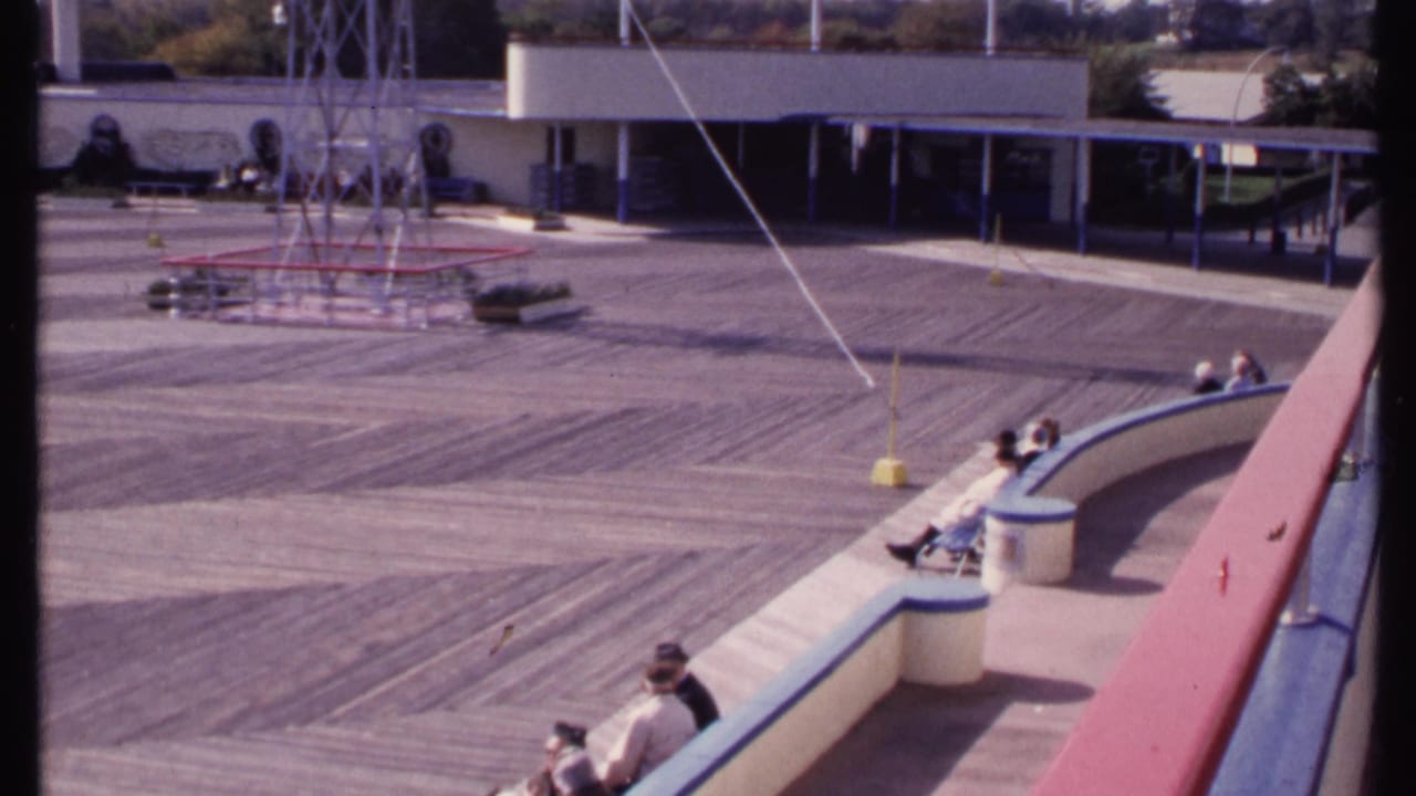 People sit on a curved outdoor bench beside a broad deck with a metal tower in the background.