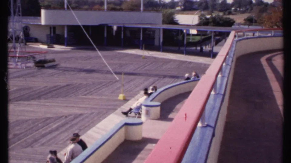 Final 1969 New London frame showing spectators along curved seating beside a sunlit deck and partial metal tower structure.