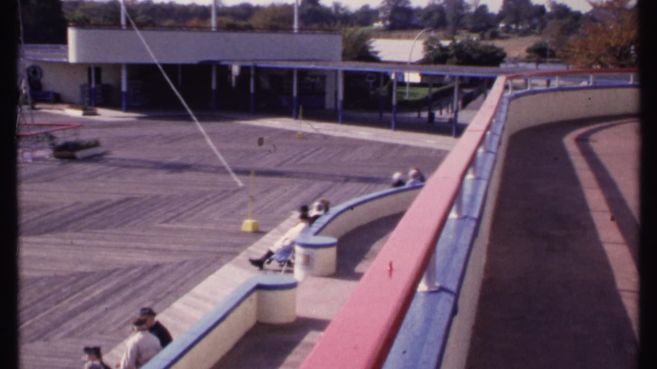 Elevated view of a curved railing beside a wooden deck with several people seated nearby.