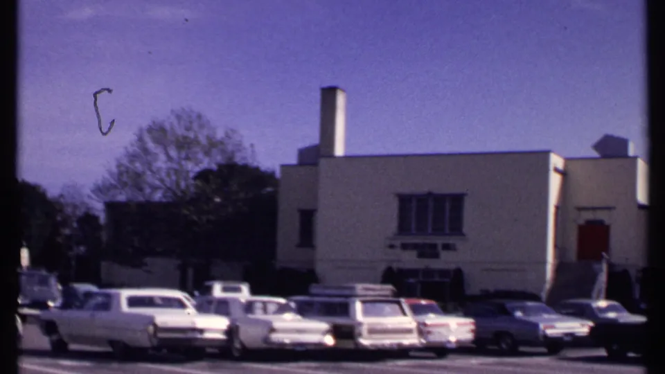 New London, Connecticut, 1969 home-movie frame showing parked sedans and wagons outside a beige recreation hall building.