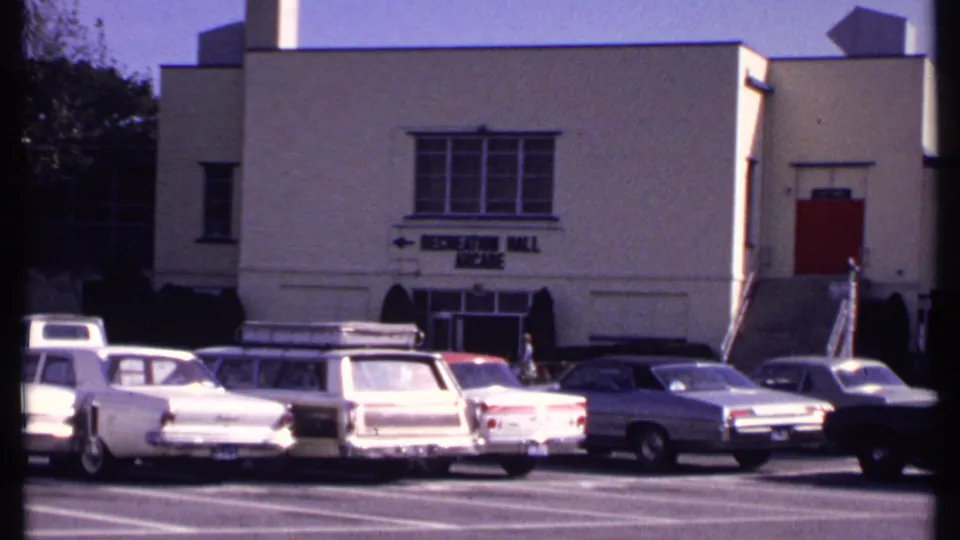 Closer 1969 New London view of parked cars, recreation hall signage, upper windows, and a red side door.