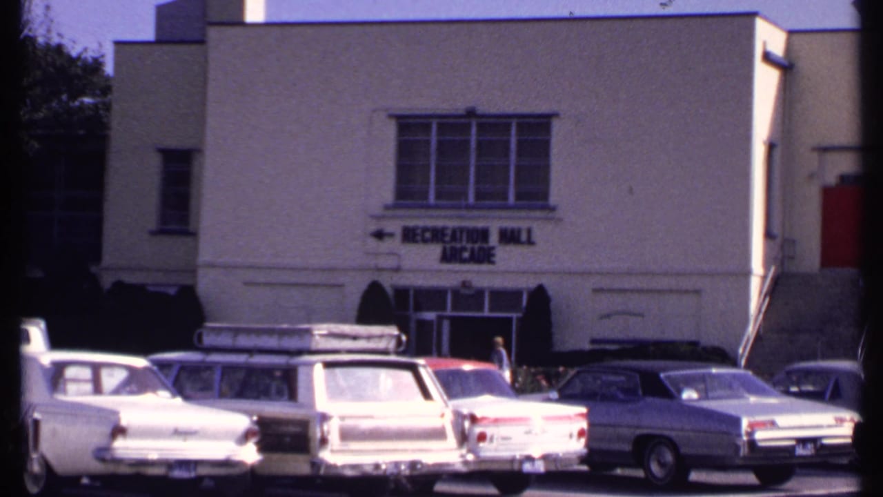 1969 New London exterior showing a white Recreation Hall Arcade building, parking lot cars, and a pedestrian near the doorway.