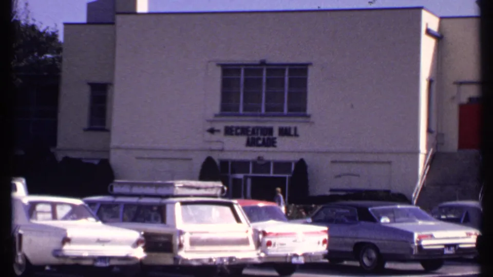 1969 New London exterior showing a white Recreation Hall Arcade building, parking lot cars, and a pedestrian near the doorway.