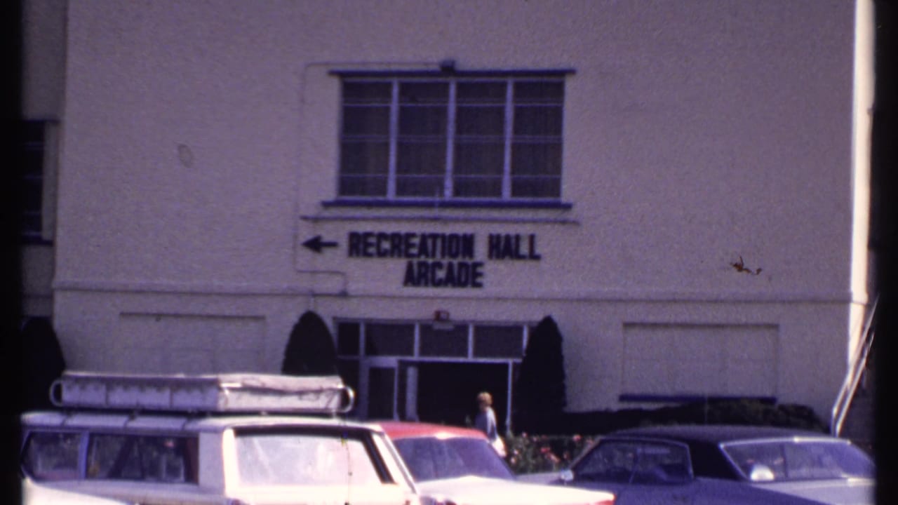 Recreation Hall Arcade sign above an entrance with parked cars and a person walking nearby.