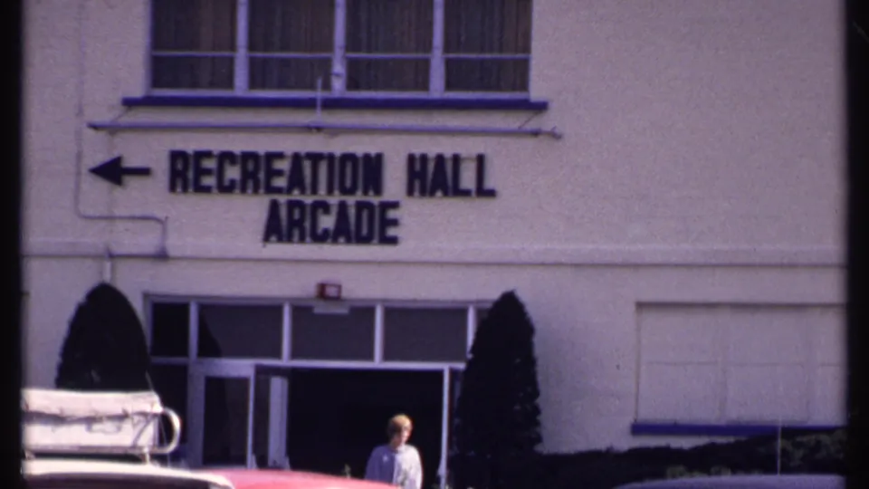 Tight 1969 New London view of the Recreation Hall Arcade sign, doorway, parked cars, and a pedestrian in front.